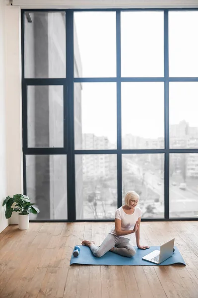 Gray-haired senior woman sitting on the floor and having a video call — 스톡 사진