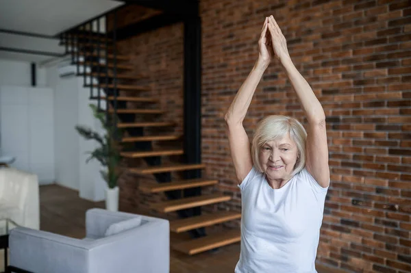 Grauhaarige Seniorin steht mit erhobenen Armen da — Stockfoto