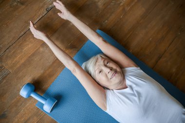 A senior woman laying on the floor and stretching