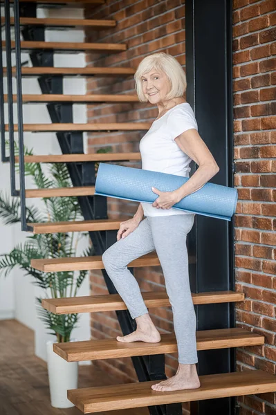 Slim senior woman with yoga mat in hands — Stockfoto