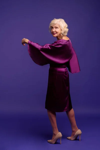 Beautiful senior blonde woman in an evening violet dress looking enjoyed — Stock fotografie