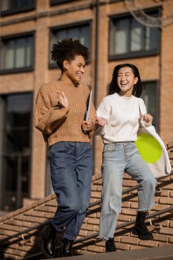 İki kız merdivenleri çıkarken mutlu mesut iletişim kuruyor.