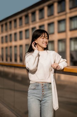 Binanın arka planında duran kız saçına dokunuyor.