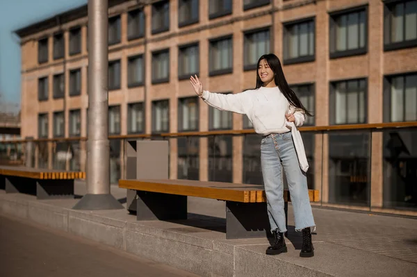 Meisje staat in de buurt bank met opgeheven hand in begroeting — Stockfoto