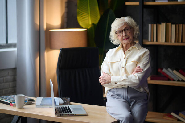 Женщина сидит на столе и уверенно смотрит в камеру.