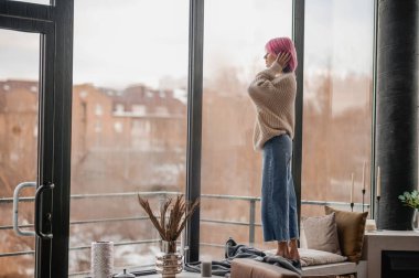 Pencerenin yanında duran pembe saçlı bir kız.