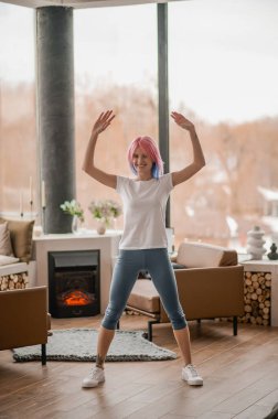 Pembe saçlı bir kız evde egzersiz yapıyor.