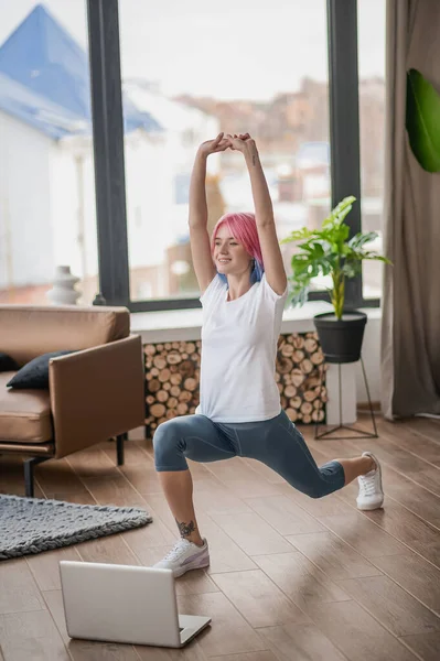 Uma menina em uma tshirt branca fazendo lunges e olhando concentrado — Fotografia de Stock