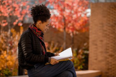 Elinde kitaplarla bankta oturan esmer tenli kız.