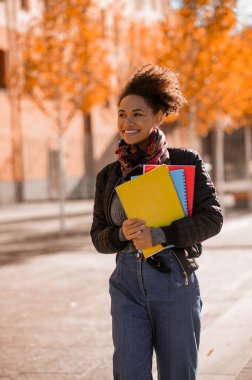 Elinde kitaplarla sokakta yürüyen bir kız.