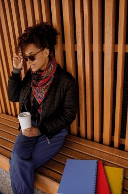 Elinde dökülmemiş bardakla güneş gözlüklü esmer bir kız.