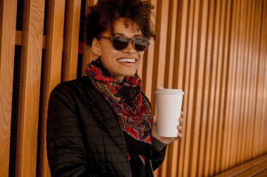 Elinde dökülmemiş bardakla güneş gözlüklü esmer bir kız.