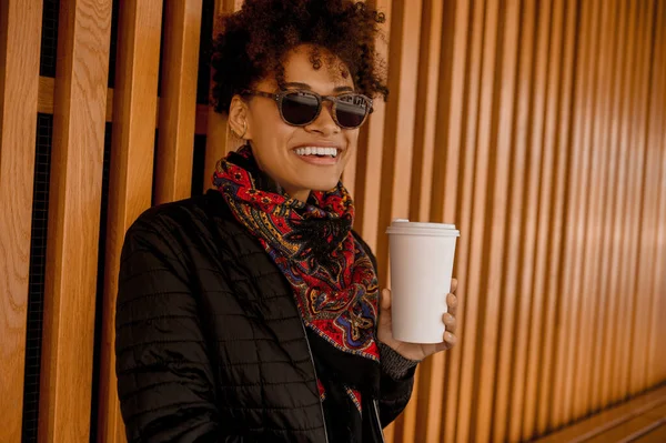 Elinde dökülmemiş bardakla güneş gözlüklü esmer bir kız.