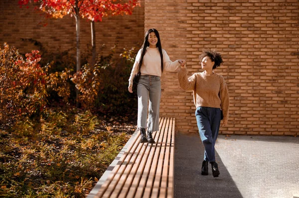 Kıvırcık saçlı kız bankta yürürken arkadaşının elini tutuyor. — Stok fotoğraf