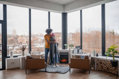 Uzun boylu genç bir adam kız arkadaşına sarılıyor ve onu ekoseyle örtüyor.