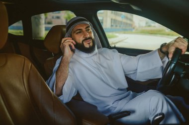 Suudi bir adam arabada oturuyor ve telefonla konuşuyor.