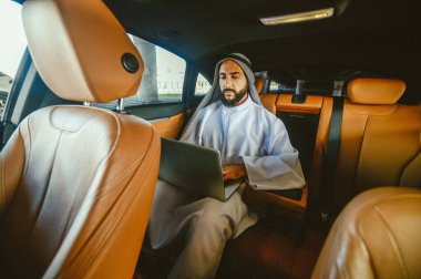 Suadi bir iş adamı bir arabada dizüstü bilgisayarla çalışıyor.