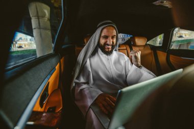 Suadi bir iş adamı bir arabada dizüstü bilgisayarla çalışıyor.