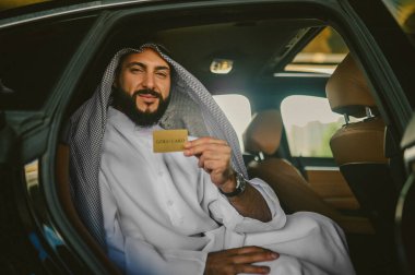 Geleneksel giysiler içinde, elinde kredi kartı olan Arap bir adam.