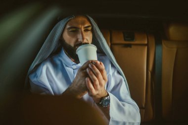 Geleneksel Arap kıyafetli bir adam arabada.