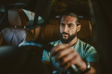 Genç, yakışıklı, koyu renk saçlı adam araba kullanıyor.