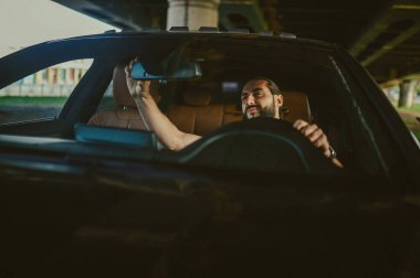 Genç, yakışıklı, koyu renk saçlı adam araba kullanıyor.