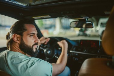 Genç, yakışıklı, siyah saçlı, elinde direksiyon tutan adam.