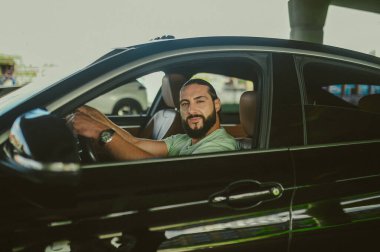 Genç bir esmer arabada oturuyor ve kendinden emin görünüyor.