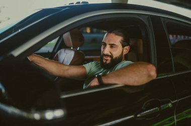 Genç bir esmer arabada oturuyor ve kendinden emin görünüyor.