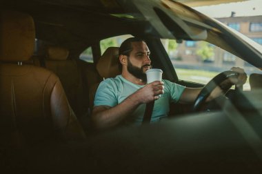 Genç bir esmer arabada oturuyor ve kendinden emin görünüyor.