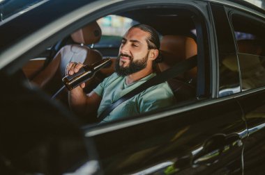 Genç, siyah saçlı, yakışıklı bir adam araba kullanıyor ve gülümsüyor.