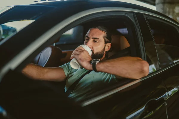 Ung brunett sitter i en bil och dricker kaffe — Stockfoto