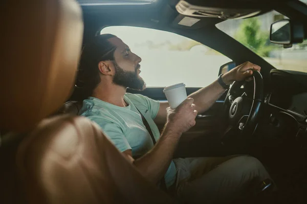 Joven hombre guapo de pelo oscuro sosteniendo un teléfono y conduciendo un coche — Foto de Stock