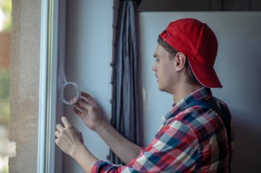 Kapak ustası plastik pencere çerçevesine bandı yapıştırıyor.