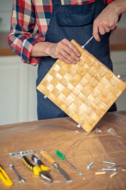 Önlüklü yetenekli bir ahşap işçisinin, metal bir menteşeyi tornavidayla kutunun kenarına vidalarken çekilmiş fotoğrafı.