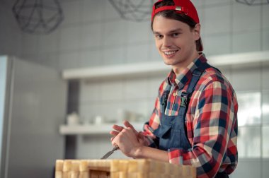 Neşeli bir marangozun belden yukarı portresi keskiyi kutunun kenarından geçirirken gülümsüyor.