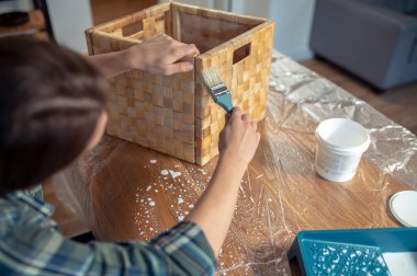 Masaya oturmuş saman kutusuna bir kat boya süren bir zanaatkârın kesilmiş fotoğrafı.