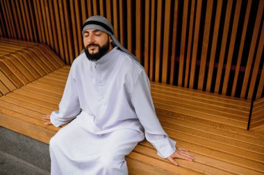 Huzurlu bir ruh hali. Genç Arap adam gözleri kapalı, huzurlu bir şekilde oturuyor.