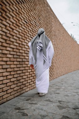 Arap adam. Geleneksel Arap başlıklı bir adam tuğla duvarın yanında duruyor.
