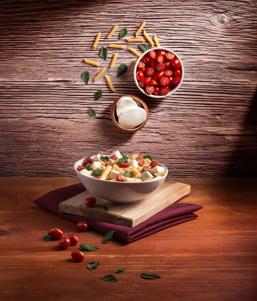 İtalyan rigatoni makarnası, beyaz tabakta beyaz domatesler ahşap ve fesleğen, reklam havalanması için malzemeler, insan yok.