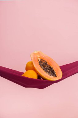 İki portakal ve bir papaya, şeftali arkaplanının önünde kırmızı bir bez üzerinde, pelvis zemininin sembolü olarak ikiye bölünmüş, insan yok.