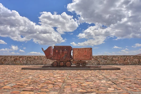 old mining car on stone patio with blue sky in the background, no peopl