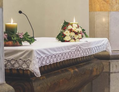 Katolik kilisesinde mum ve çiçeklerle sunak resmi.