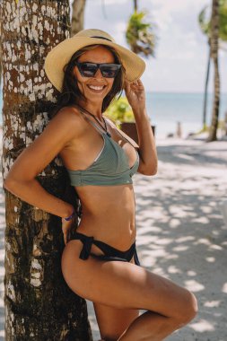 Cennet sahilinde palmiye ağaçlarıyla bikini giymiş bir kadın model.