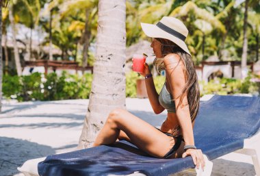 Tropik bir plajda bikinili bir kadın poz veriyor.