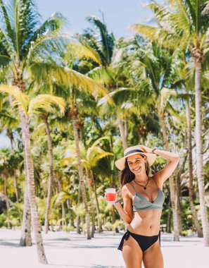 Tropik bir plajda bikinili bir kadın poz veriyor.