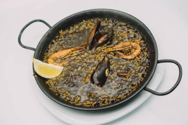 Bir tabak siyah pirinç paella ile kalamar, karides ve midye.