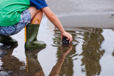 Çocuk bir yeşil Boots göletlerde atlama. Bir çocuk yağmur, parlak bir yağmurluk duruyor. Sonbahar park oynayan çocuk. Herhangi bir hava açık eğlence