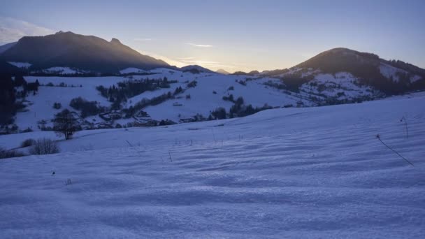 Zimowa wioska w dolinie po zachodzie słońca, ośnieżone wzgórza, mroźne temperatury — Wideo stockowe