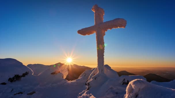 Ein gefrorenes christliches Kreuz in den Winterbergen bei der untergehenden Sonne. Sonnenuntergang — Stockvideo
